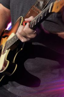 Man in black shirt playing a brown electric guitar