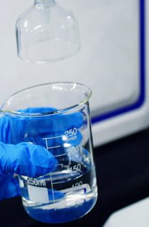 Blue glove holding glass beaker