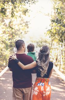 Young family walking in a light forest and carrying their toddler