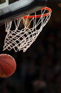 Basketball in the air underneath a basketball hoop