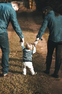 Young family walking a green forest and holding hands with their toddler